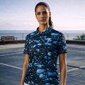 Woman in a blue patterned shirt and white skirt standing on a tennis court.